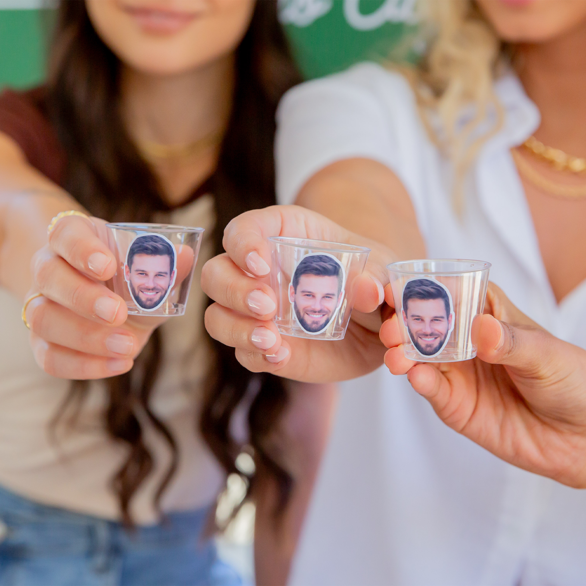 Girls at a Bachelorette or Birthday Party holding 3 clear personalized plastic shot glasses with a friends face on it.