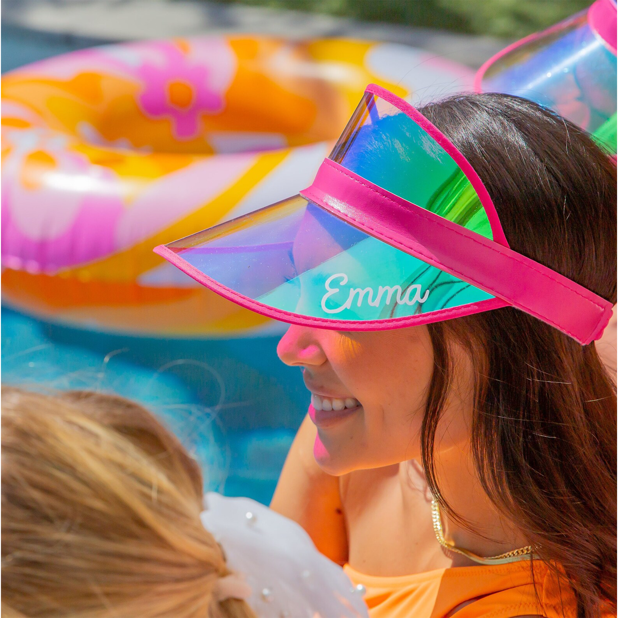 Bridesmaid wearing a personalized pink holographic visor at a pool bachelorette party with colorful party supplies—fun custom party accessory.