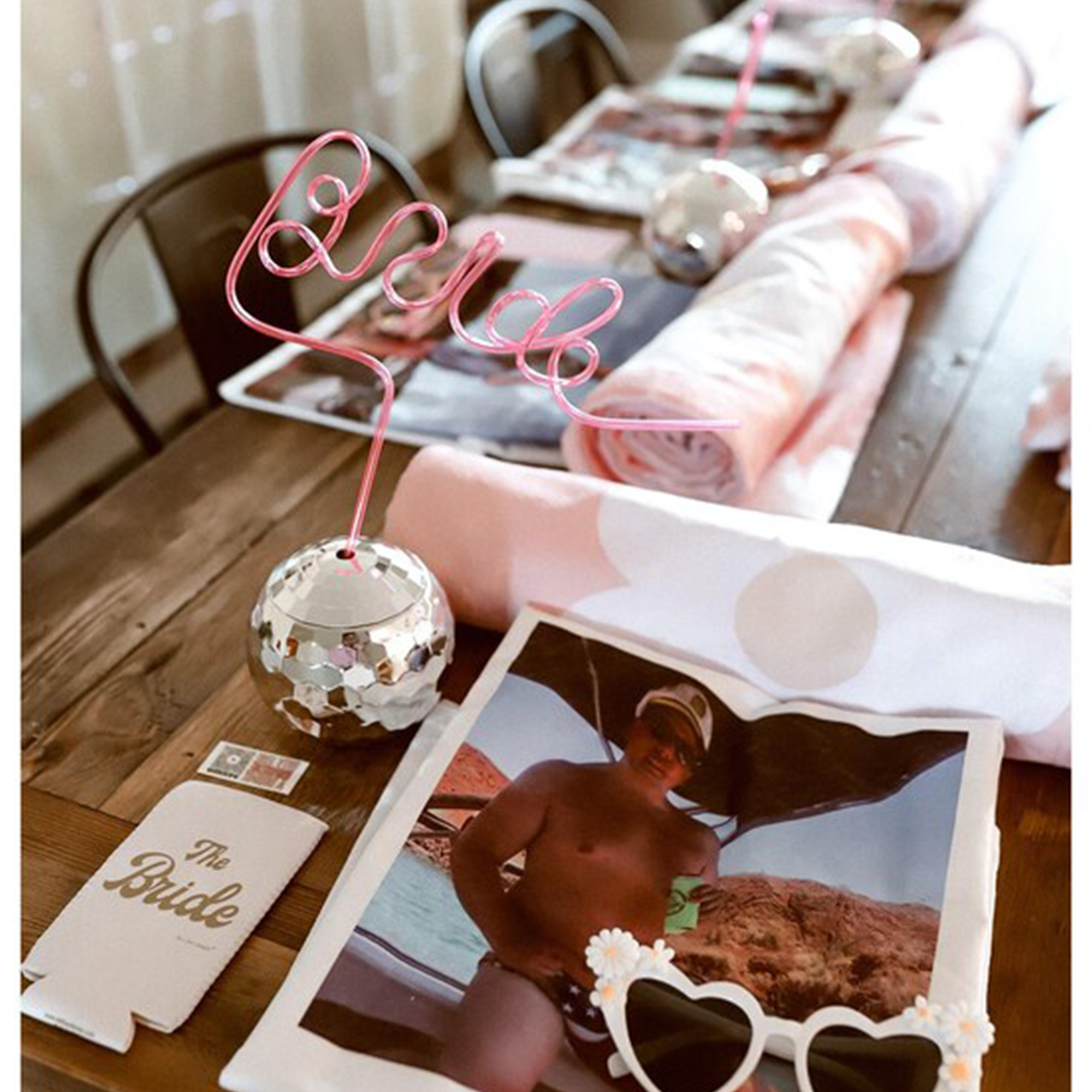 Bridesmaid bachelorette party favors on a table—fun heart sunglasses, custom tattoos, chrome disco ball drinkware, and a hot pink 'Bride' straw for photo-ready party decor.